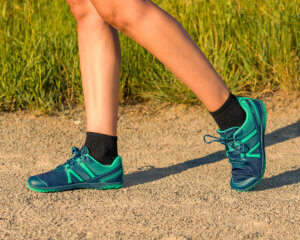 A close up shot of a woman walking in her HFS II barefoot shoes on a dirt road